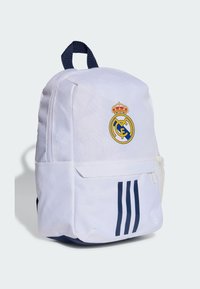 Bijela ruksak s plavim akcentima, na kojem se nalazi logo Real Madrida i tri tamnoplave pruge sprijeda. Izrađen od izdržljive tkanine.