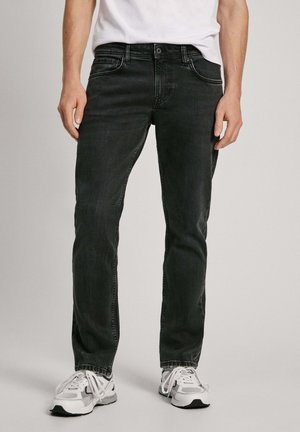 Mustad denim püksid sirge lõikega, viie taskuga ja õmblusdetailidega, koos valgete treeningjalatsitega.