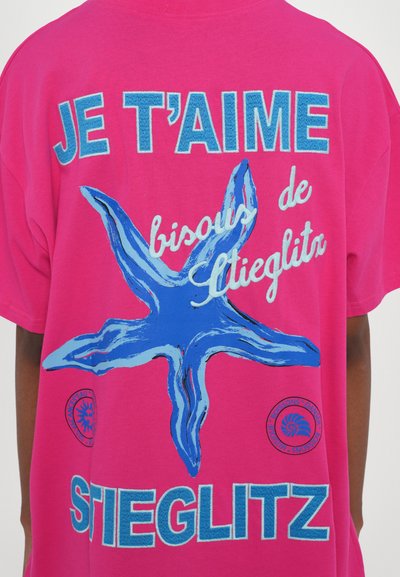 Roza bombažna majica z velikim modrim morskim zvezdnikom, besedilom v beli in modri barvi "JE T’AIME bisou de Stieglitz" ter krožnim logotipom.