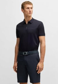 Granatowa koszulka polo z zamkiem, z fakturowanym wzorem. Po�łączona z granatowymi szortami i wzorzystym ciemnym paskiem, wszystkie w dopasowanych odcieniach.