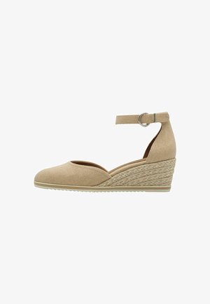 Beige canvas wedge schoen met enkelbandje, ronde neus en geweven jute details op de hak. Platte rubberen zool voor grip.