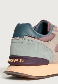 Zapatilla con parte superior de ante verde, acentos de cuero en color teal y una mediasuela púrpura. Presenta costuras distintivas y una suela texturizada.