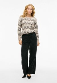 Pletena džemper s cik-cak uzorkom u bež, crnoj i smeđoj boji; kombiniran s visoko strukiranim crnim kordura hlačama i crnim štiklama.