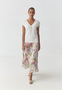 Top bianco con scollatura a V abbinato a una gonna fluida e plissettata con stampa floreale in rosa, giallo e verde. Modella che indossa sandali bianchi.
