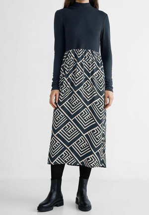 Robe à manches longues avec un haut bleu marine et une jupe à motifs en formes géométriques beiges. Fabriquée en tissu doux, elle présente un haut ajusté et un bas évasé.
