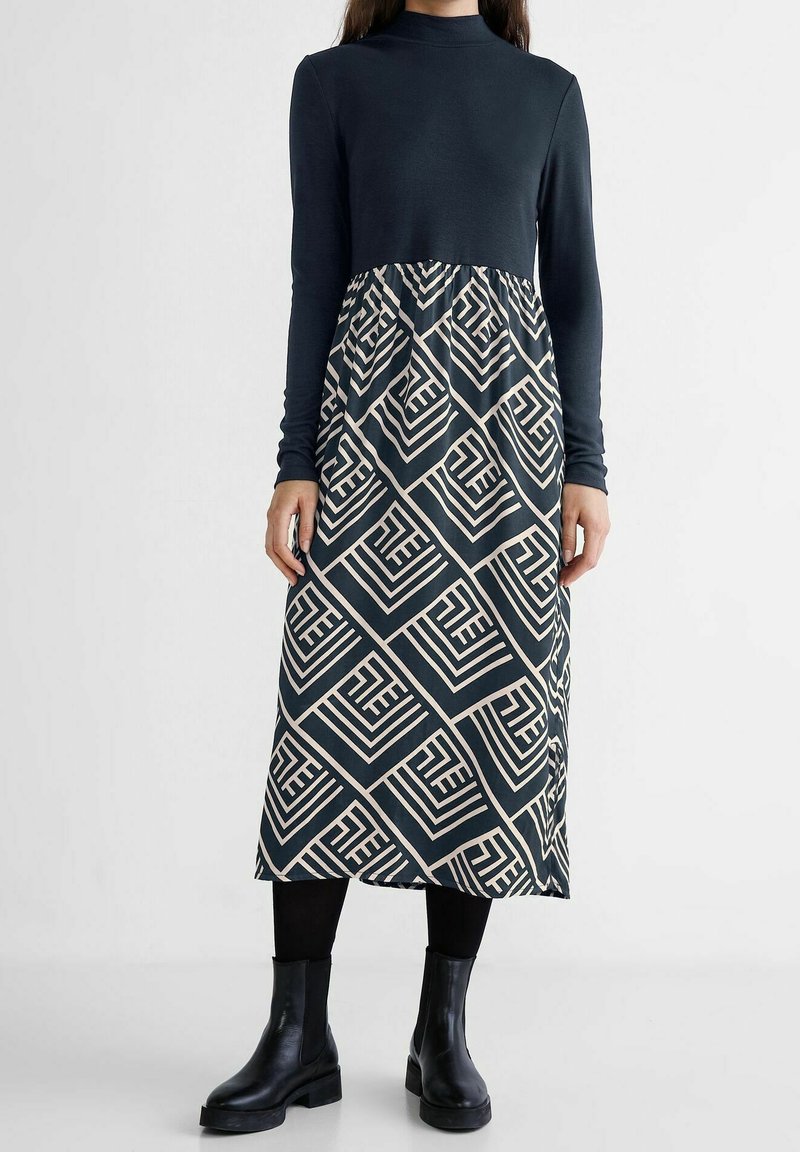 Dlouhé šaty s námořnickým vrškem a vzorovanou sukní v geometrických béžových tvarech. Vyrobeny z měkké tkaniny, s přiléhavým vrškem a rozšířeným spodním dílem.
