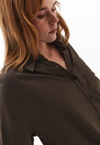 Camicia marrone con bottoni realizzata in un tessuto morbido; presenta una vestibilità comoda, colletto, dettagli sulla tasca e una sottile texture.