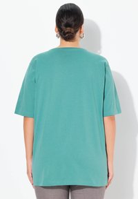 Türkises Baumwoll-T-Shirt mit kurzen Ärmeln, lockerer Passform und Rundhalsausschnitt. Glatte Textur, keine sichtbaren Muster oder Akzente.