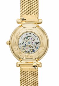 Fossil Automatikuhr mit einem goldenen Edelstahl-Mesh-Armband, transparentem Gehäuseboden, der das komplizierte Werk zeigt, akzentuiert mit bunten Zahnrädern.