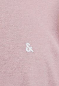 Lyserødt bomuldsstof med en fin struktur har et hvidt broderet ampersand-symbol nederst til venstre.
