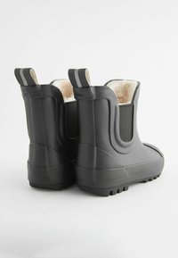 Bottes en caoutchouc noires pour la cheville avec une semelle texturée, des panneaux latéraux élastiques et une doublure en fourrure douce visible en haut, dotées de languettes pour un enfilage facile.