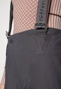Black overalls with adjustable gray straps featuring red accents. Textured fabric with a smooth finish and side button detail.