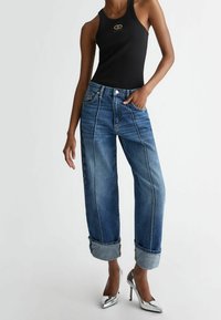 Džíny z denimu, modré s lehkým vyblednutím, mají ohrnuté lemy, rovný střih nohavic a kontrastní švy. Kombinovány s černým tílkem bez rukávů.