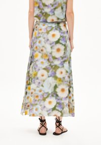 Vloeiende maxi rok met grote bloemenprint in zachte kleuren, met een zijopening en gecombineerd met platte zwarte sandalen, verstelbare bandjes.