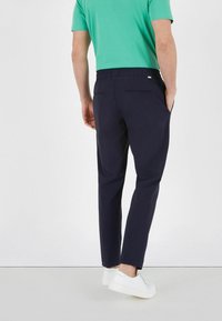 Mørkeblå bukser med en glat overflade, tapered ben og elastisk talje. Kombineret med en grøn skjorte og hvide sneakers.