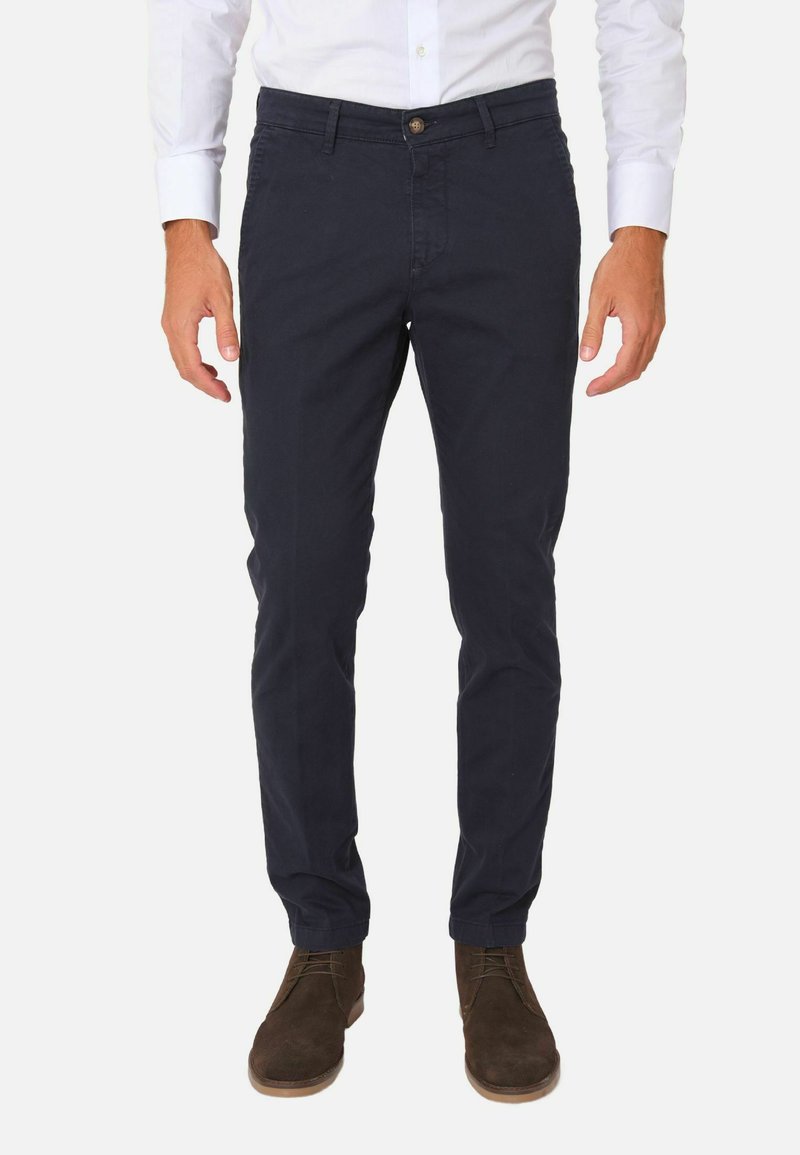 Chinos blu navy, slim fit, in cotone, con chiusura a bottone e tasche frontali, abbinati a stivaletti alla caviglia in suede marrone.
