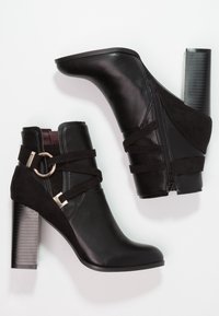 Botas negras hasta el tobillo con una mezcla de cuero liso y ante. Cuentan con un cierre de cremallera, una hebilla llamativa y un tacón negro grueso y estriado.