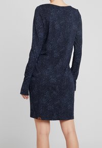 Mörkblå långärmad klänning med ett texturerat mönster av små ljusblå prickar, med rundad halsringning och en märkessöm som accent.