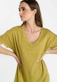 Olijfgroen oversized t-shirt van zachte stof, met een v-hals en korte mouwen, voorzien van een subtiel logo aan de linkerkant.