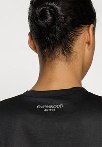 Schwarzes Sportoberteil mit strukturierter Oberfläche, rundem Ausschnitt und Logo "even&odd ACTIVE" auf der Rückseite.