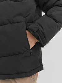 Giubbotto imbottito nero con tasca laterale con zip e polsini in Velcro. Il tessuto ha una texture liscia con un design trapuntato per l'isolamento.