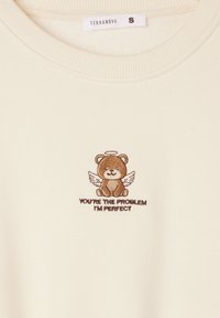 Felpa color crema con colletto e orlo a coste, decorata con un orso marrone ricamato con le ali e la scritta "SEI TU IL PROBLEMA, IO SONO PERFETTO."