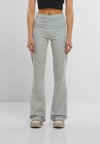 Pantaloni grigi chiari a campana con una larga vita piegata. Realizzati in materiale morbido ed elasticizzato. Abbinati a scarpe da ginnastica beige.