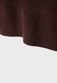 Burgundy strikstof med en blød tekstur, der har en let bølget kant. Materialet ser tykt og hyggeligt ud, ideelt til koldere vejr.