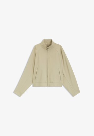 Giacca beige con cerniera, collo alto e due bottoni, maniche lunghe e tasche frontali a fessura, stesa su sfondo bianco.