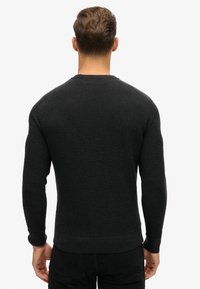 Suéter negro texturizado con un patrón acanalado, mangas largas y cuello de barco. Los puños ajustados y el dobladillo de la cintura aportan estructura.