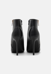 Botines de cuero negro con tacón de aguja, detalle de cremallera en la parte trasera y textura lisa. Interior forrado y diseño minimalista.