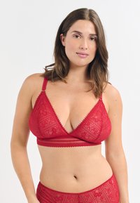 Bralette en dentelle rouge de forme triangulaire, ornée de motifs floraux complexes, avec des bretelles ajustables et une large bande sous la poitrine.