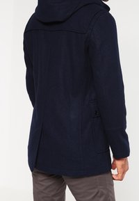 Navy-blandad ullkappa med huva, framfickor och rak skärning. Texturen är slät med en matt finish.