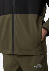 Μπουφάν σε ελιά πράσινο και μαύρο με φερμουάρ μπροστά, με σχεδιασμό αντίθετων πάνελ και διακριτικό λογότυπο στο κάτω δεξί μέρος. Ομαλή υφή.