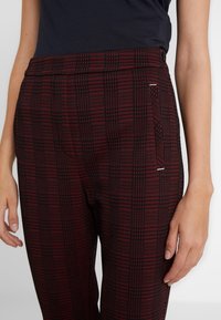 Červené a černé kostkované kalhoty vyrobené z tkané látky. Mají plochý přední střih a boční kapsy s jemným bílým akcentem.