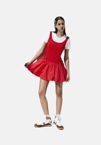Rode uitlopende jurk met een aansluitend lijfje en eenGathered taille, gecombineerd met een wit T-shirt en bruin-witte sneakers. Glad stofoppervlak.