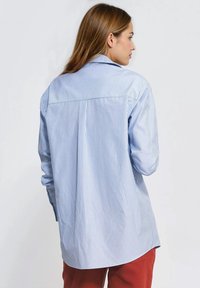 Koszula na guziki w niebiesko-białe paski, z długimi rękawami, tylnym karczkiem i zaokrąglonym dołem. Wykonana z lekkiego materiału.