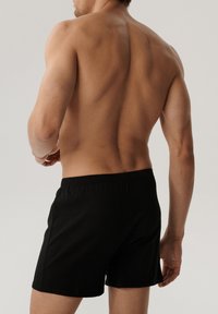 Czarne bokserki z elastycznym pasem, widoczne od tyłu, pokazujące gładką teksturę materiału oraz prosty, klasyczny design.
