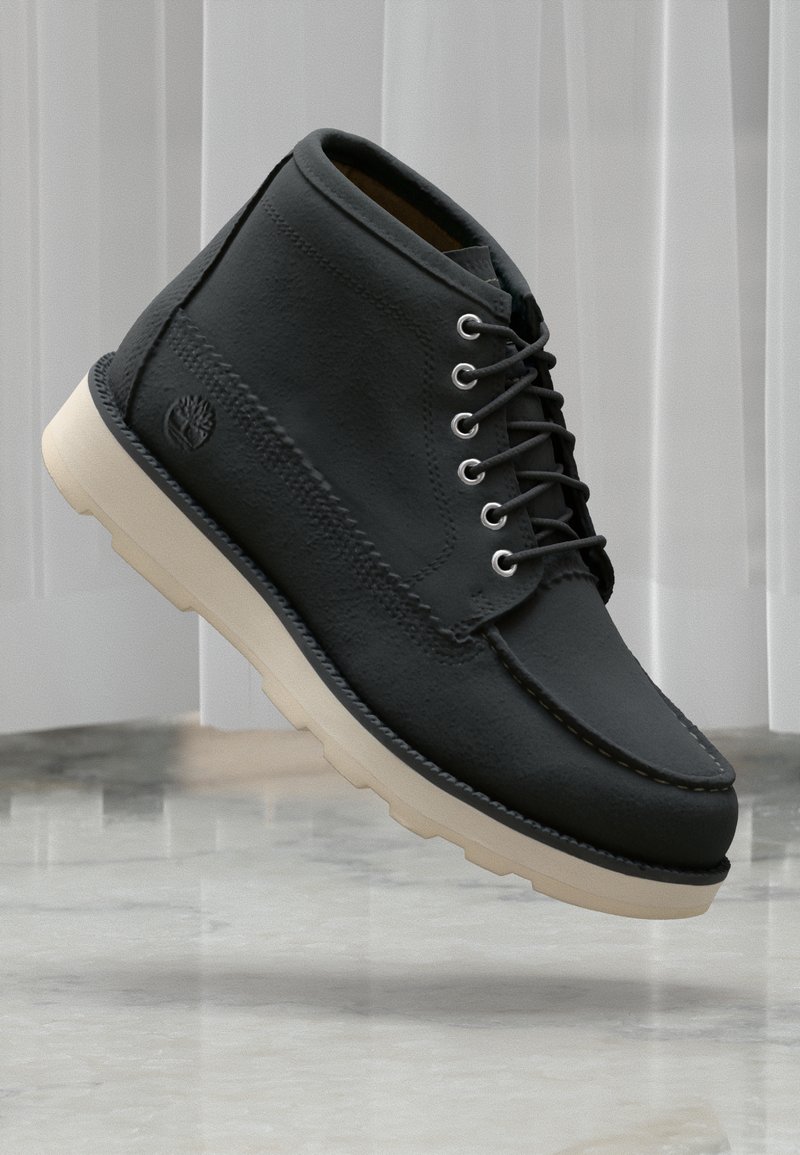 Black leather ankle boots with a rounded toe and white rubber sole. Features include lace-up front and subtle logo detailing on the side.