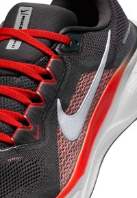 Chaussure de sport noire et rouge avec une tige en mesh texturé, un logo Nike en argent, des lacets rouges plats et une semelle épaisse blanche avec des accents rouges.