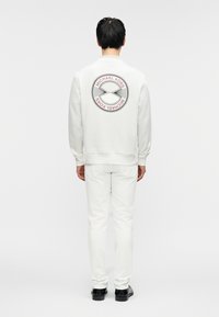 Λευκό φούτερ με στρογγυλό λογότυπο στο πίσω μέρος, με το κείμενο "Michael Kors", συνδυασμένο με λευκό παντελόνι και μαύρα παπούτσια. Ομαλή υφή.