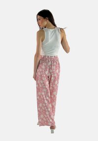 Witte mouwloze top gecombineerd met roze bloemenpatroon broeken met een elastische tailleband. De broeken hebben een losse, wijde pasvorm.