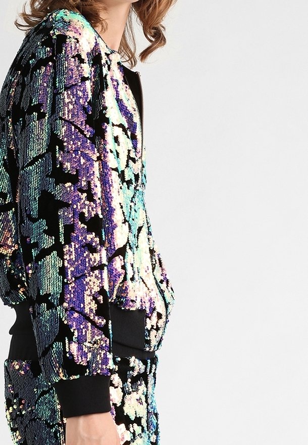 Veste bomber à sequins aux teintes multicolores de violet, turquoise et vert avec des accents noirs. Comprend une fermeture éclair et des poignets côtelés.