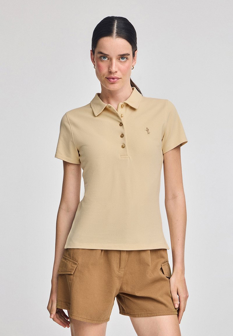 Beżowa koszulka polo z kołnierzykiem, wyposażona w pięć guzików i małe logo na klatce piersiowej. Krótkie rękawy oraz dopasowany krój.
