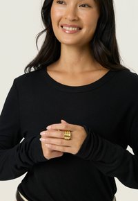 Fekete, hosszú ujjú póló kerek nyakkivágással. Puha, rugalmas anyag. A modellen arany, háromsávos gyűrű van, amely jól karbantartott kezeket mutat.