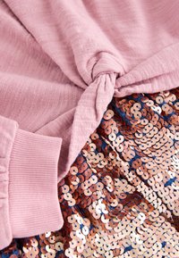 Világos rózsaszín felső csavarodott csomó részlettel, rose gold és tengerészkék kör alakú flitterekkel díszített flitteres szoknyával párosítva.