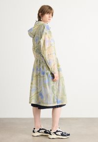 Long, hooded jacket with a textured, lightweight fabric featuring a green and blue abstract pattern. Elasticized waist, long sleeves, and pockets.