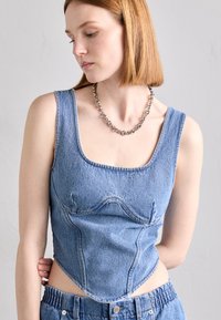 Denimist crop-top ruudulise dekoltee, struktureeritud õmblustega ja keha lähedane siluett. Komplektil on kõrge vöökoht ja helesinised denimipüksid.