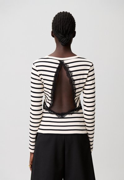 Top de manga larga a rayas en crema y negro, con un amplio escote en la espalda bordeado con encaje negro. Tejido suave con diseño ajustado.