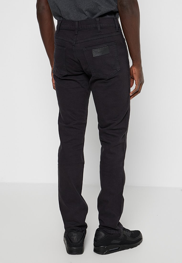 Czarne dżinsy w wąskim kroju, z etykietą na tylnej kieszeni, szlufkami na pasek i subtelnymi detalami szwów. Noszone z czarnymi trampkami.